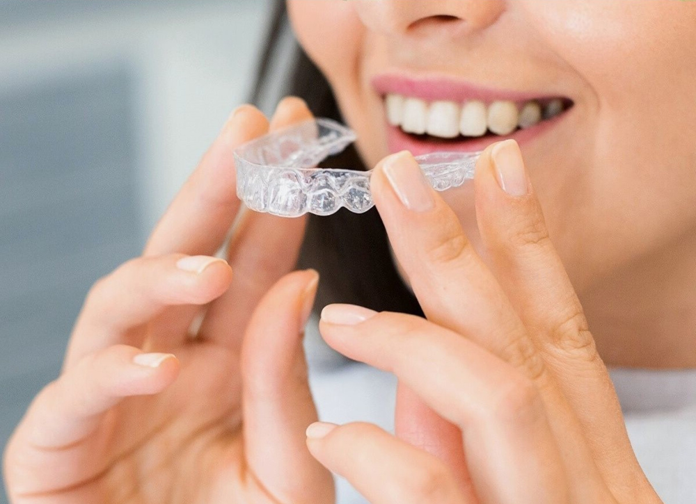 Woman holding an Invisalign aligner and smiling during clear aligner treatment in Woking